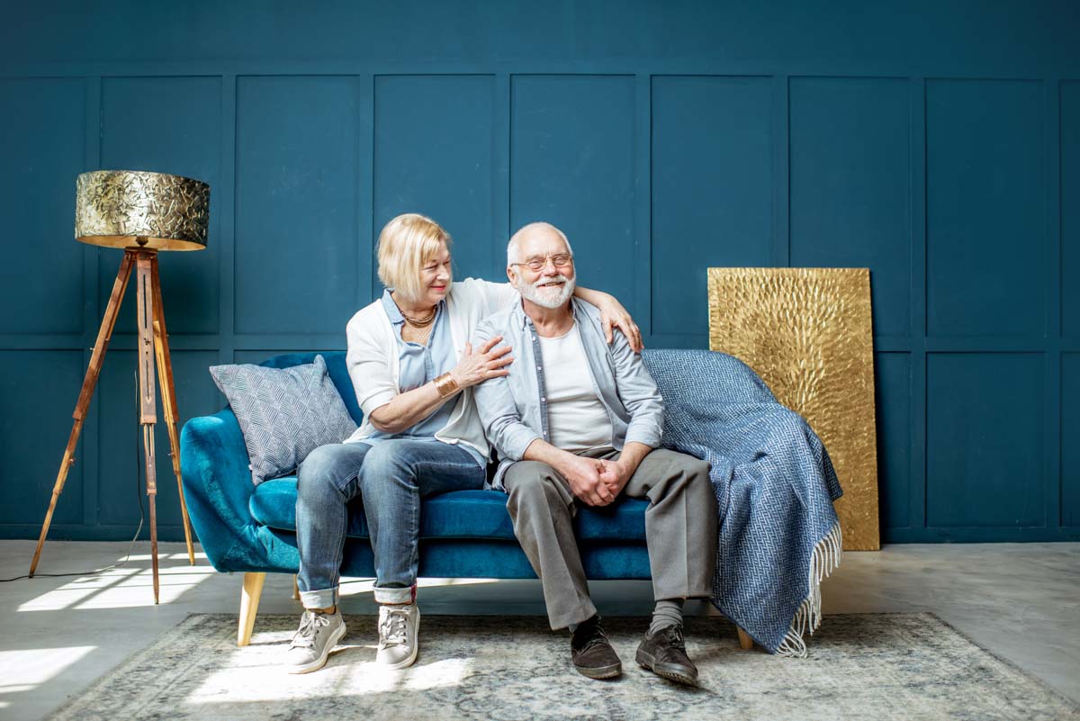 smiling elderly couple holding each other on a couch