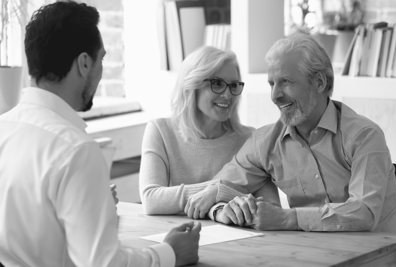 smiling elderly couple holding hands and talking to a representitive